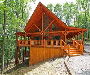 two story log cabin with tall green trees and large wrap around deck