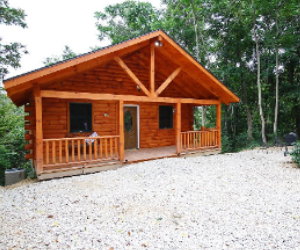 log cabin with front seating area on porch with wooded lot