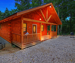 log cabin with front seating area on porch with wooded lot
