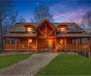 two story log cabin with wrap around porch and gravel driveway