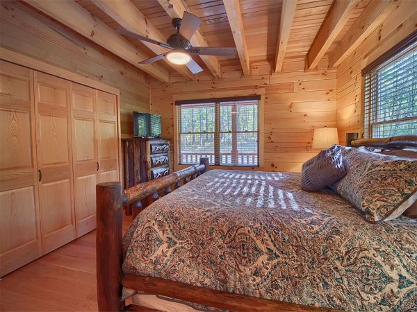 wooden bed, overhead ceiling fan, windows,  storage cabinets