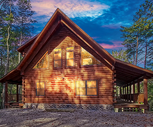 lodge on side of hill with wrap around deck. Tall wooded area around lodge.