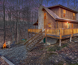 cabin side view on hill with tall stone exterior fireplace and wrap around deck