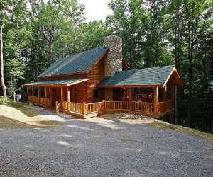 log cabin set back from road with wrap around porch and a green roof with stone fireplace